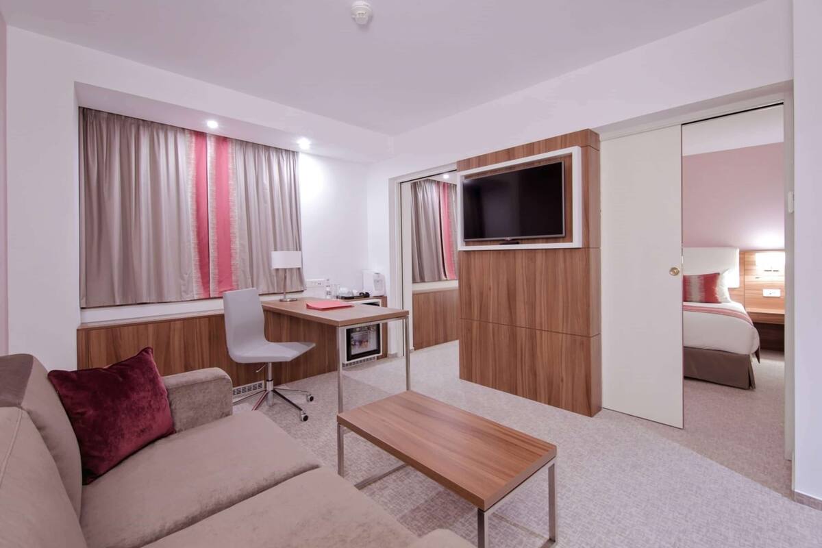 Una habitación de hotel moderna con sofá, escritorio, televisión y cama.