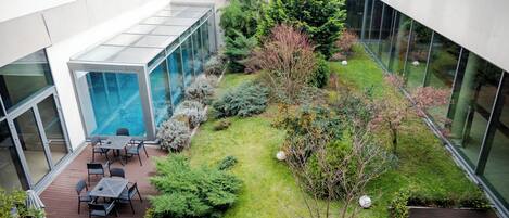 A rooftop garden with a glass enclosure, outdoor seating, and various plants.
