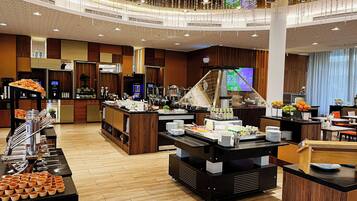 A hotel breakfast area with a buffet setup, a coffee station, and a television screen displaying a promotional offer.