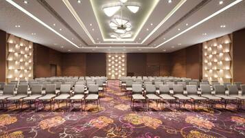 A conference room with rows of chairs, a patterned carpet, and a ceiling with recessed lighting and a central chandelier.