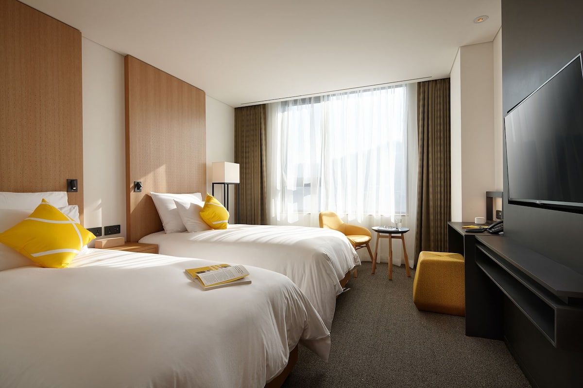 Een hotelkamer met twee bedden, een televisie, een tafeltje en een stoel.