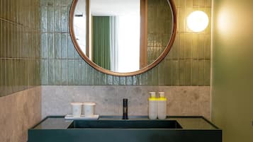 Un baño con lavamanos de vidrio, un espejo redondo y artículos de aseo en la encimera.