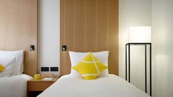 A hotel room with two beds, a wooden headboard, a bedside table with a clock, and a floor lamp.