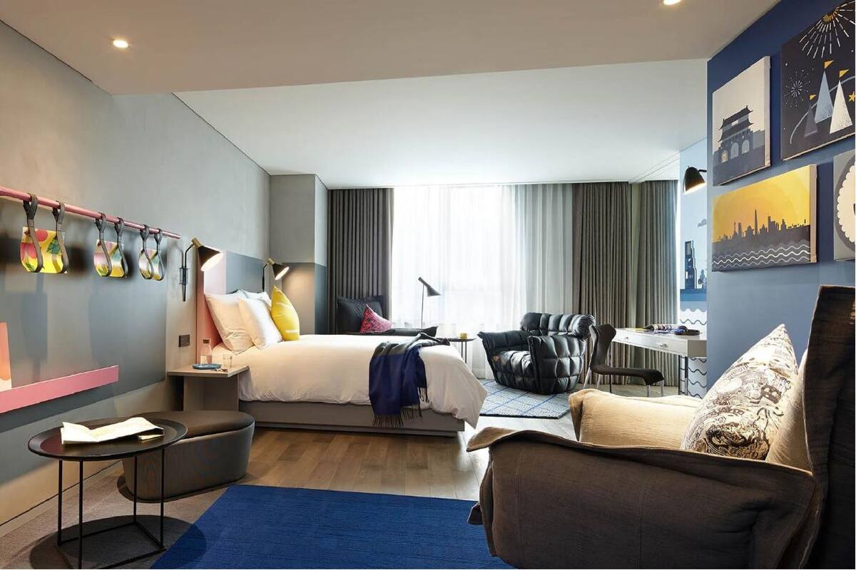 Een moderne hotelkamer met een bed, een bureau, een stoel en kunstwerken aan de wanden.