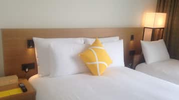 A hotel room with two beds, a nightstand with a clock, a remote control, and a lamp.