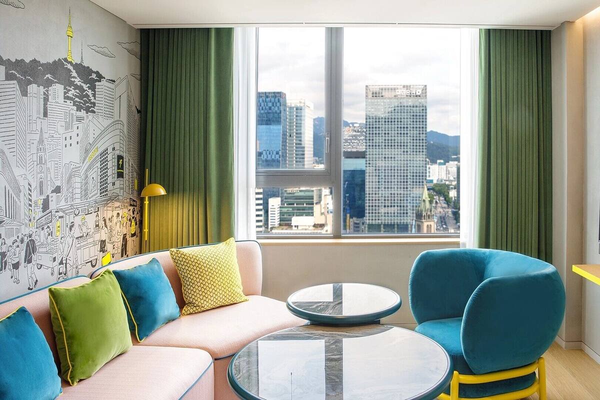 Een moderne hotelkamer met uitzicht op de stad, een bank, twee stoelen, een klein tafeltje en een groot televisiescherm.