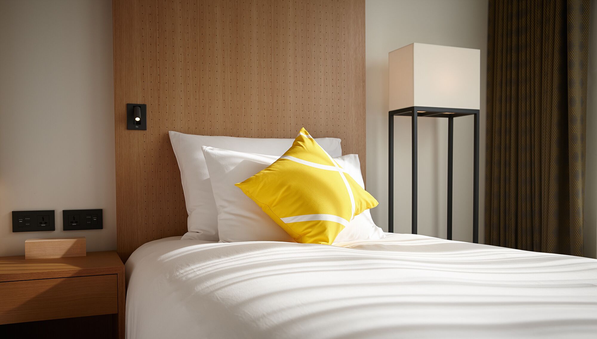 A hotel room with a bed, a nightstand, a lamp, and a wall-mounted control panel.