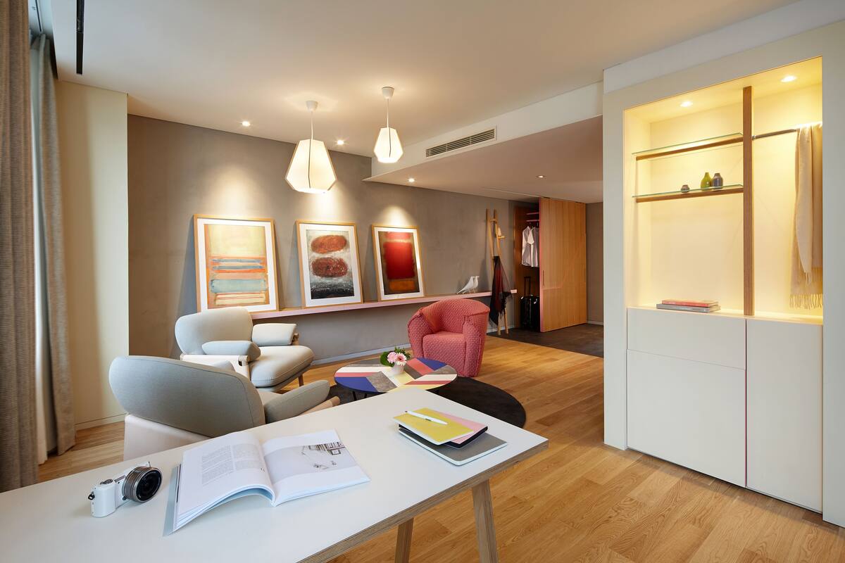 Een moderne woonkamer met een witte tafel, een camera en een open boek. Er hangen drie ingelijste kunstwerken aan de muur, een rode stoel en een houten kast met planken.