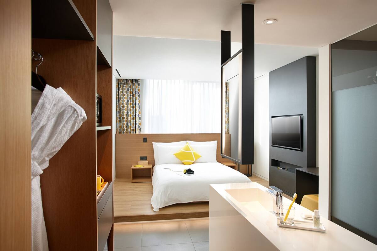 Een hotelkamer met een bed, een aan de muur bevestigde televisie, een badkamer met een wastafel en een douche.