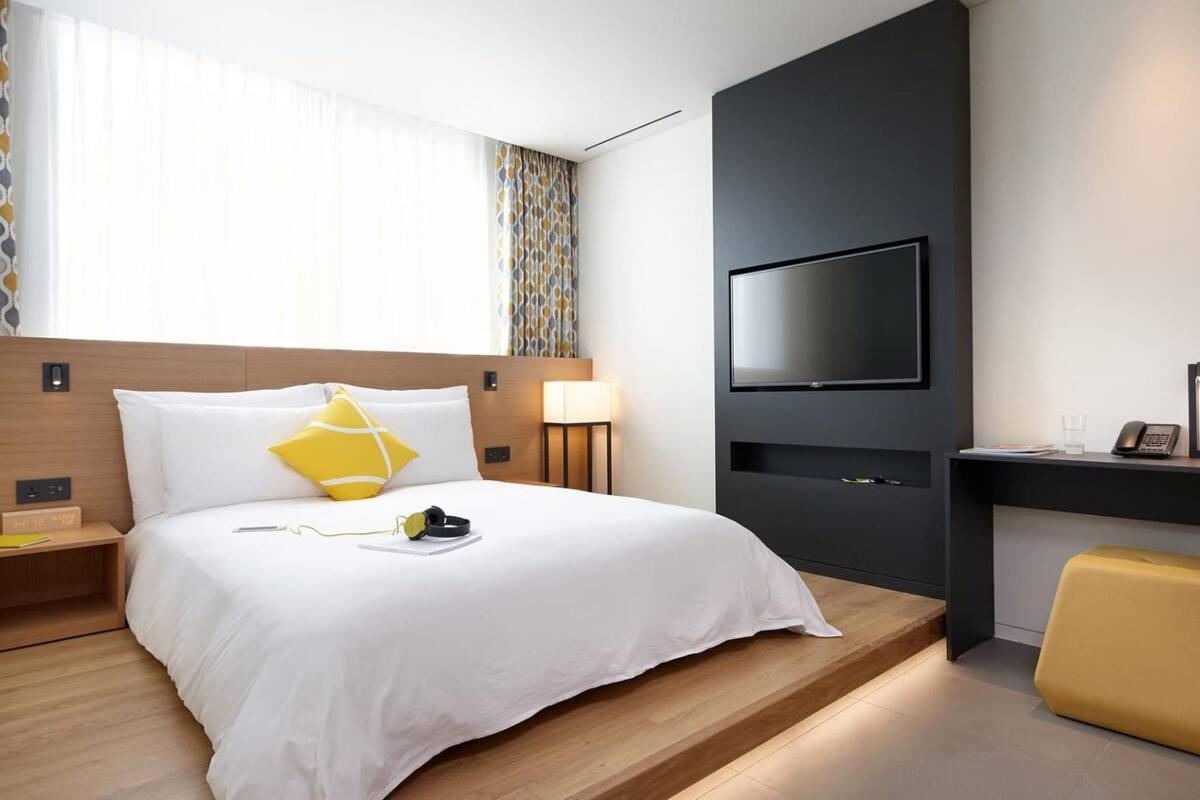 Een moderne hotelkamer met een bed, nachtkastje, lamp, televisie, bureau en stoel.