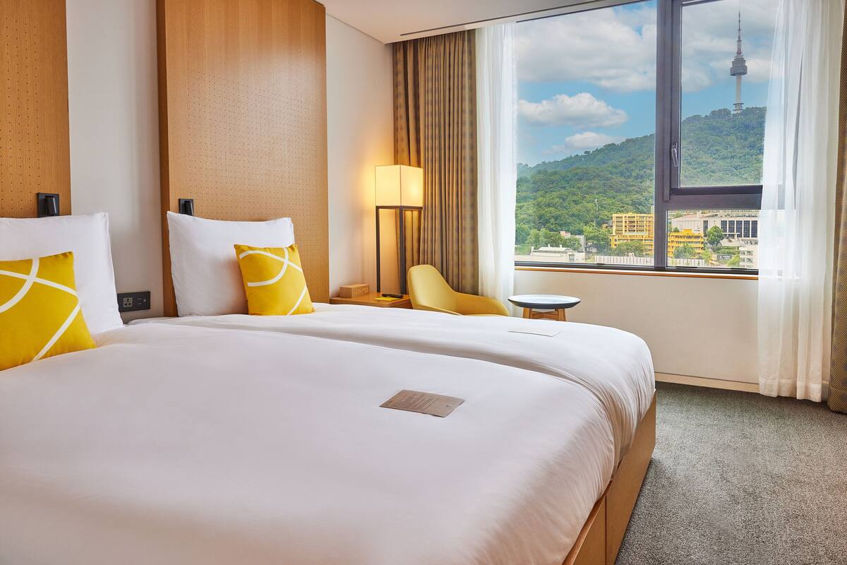 Een hotelkamer met een groot bed, een bureau, een stoel en uitzicht op een toren en groen.