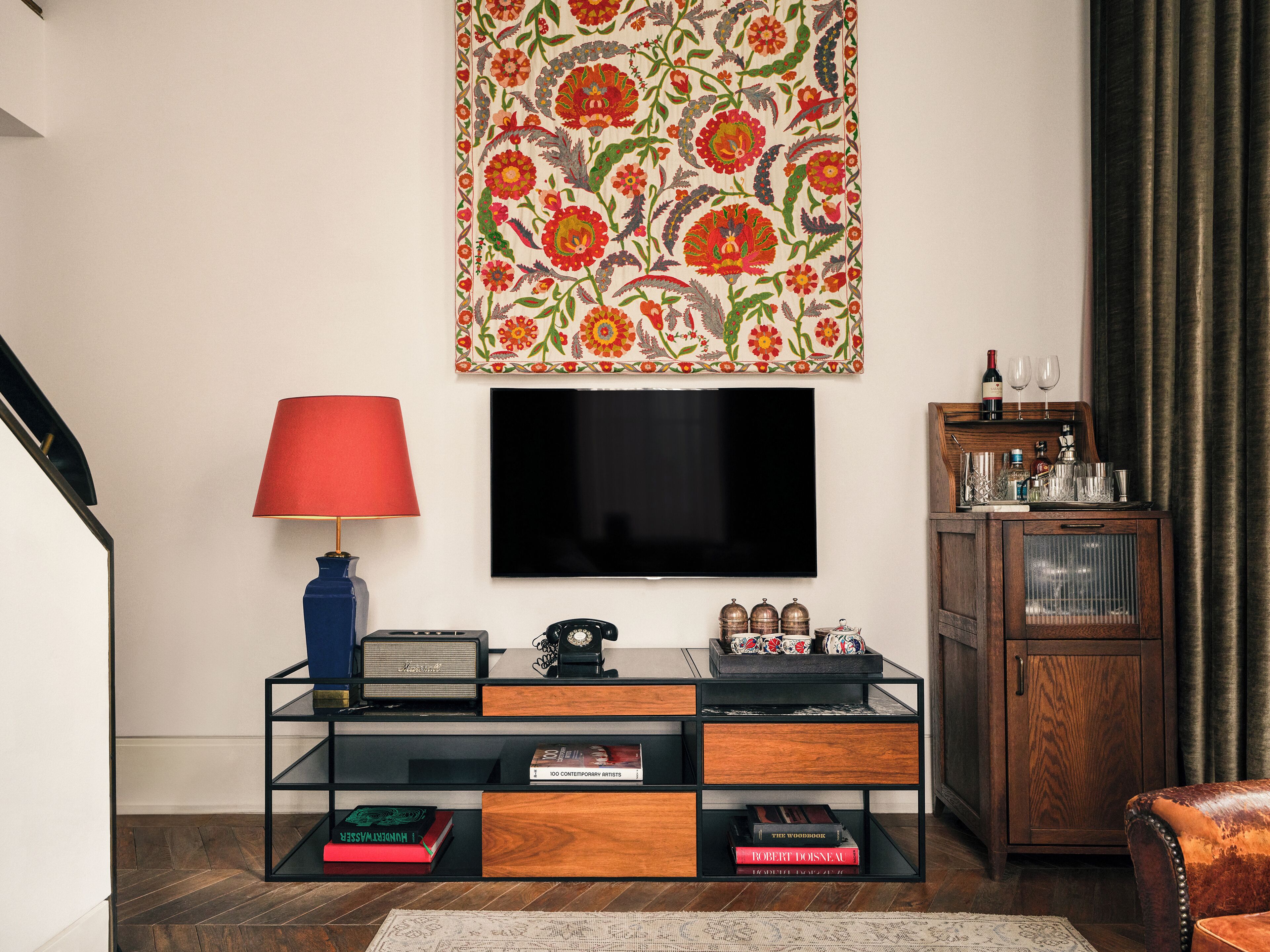 A living room with a flat-screen TV, a red lamp, a wooden cabinet, and a bookshelf with books.