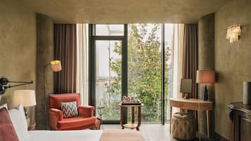 Habitación de hotel con cama, un sillón rojo, un escritorio y vistas a zonas verdes.