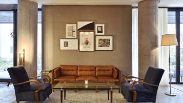 Un salon moderne avec un canapé en cuir marron, deux fauteuils, une table basse en verre et un mur décoré de tableaux encadrés.