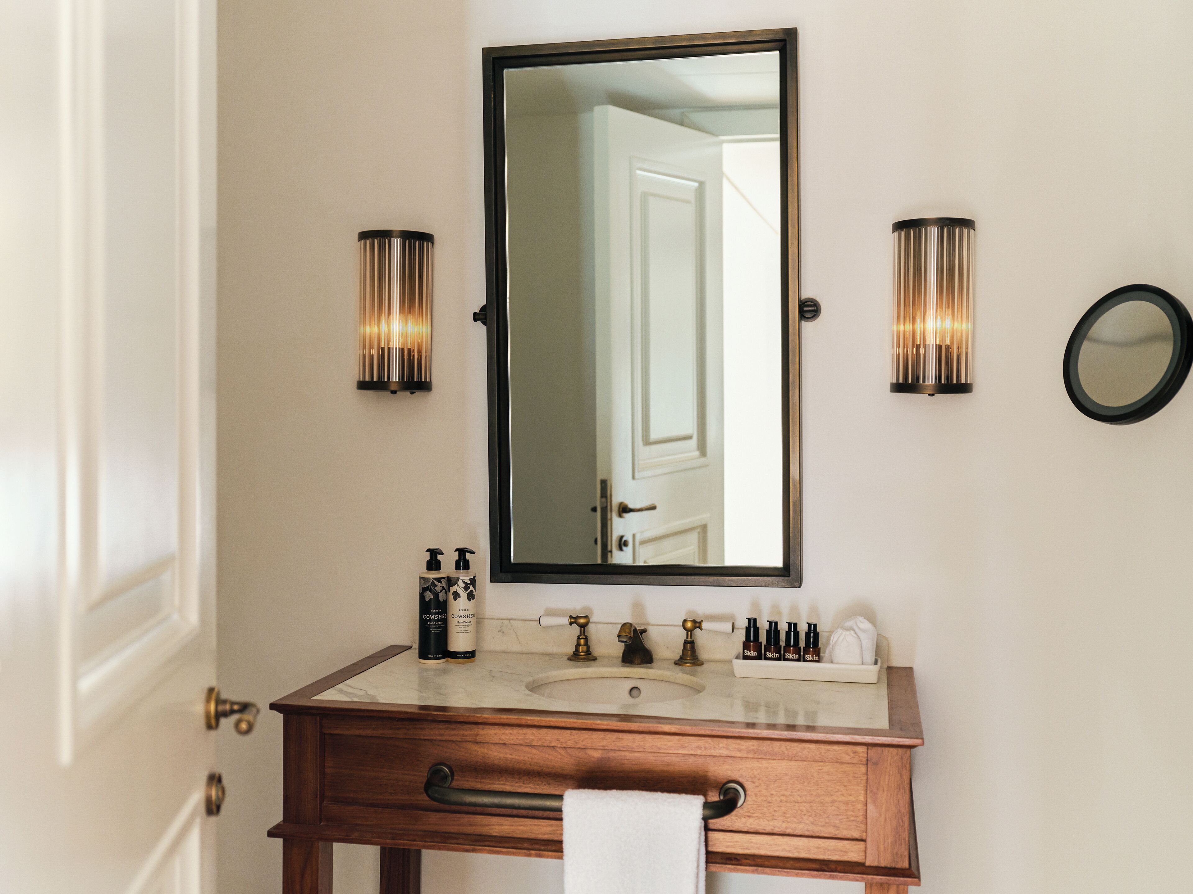 A bathroom with a wooden vanity, a large mirror, two wall-mounted lights, and a round mirror.