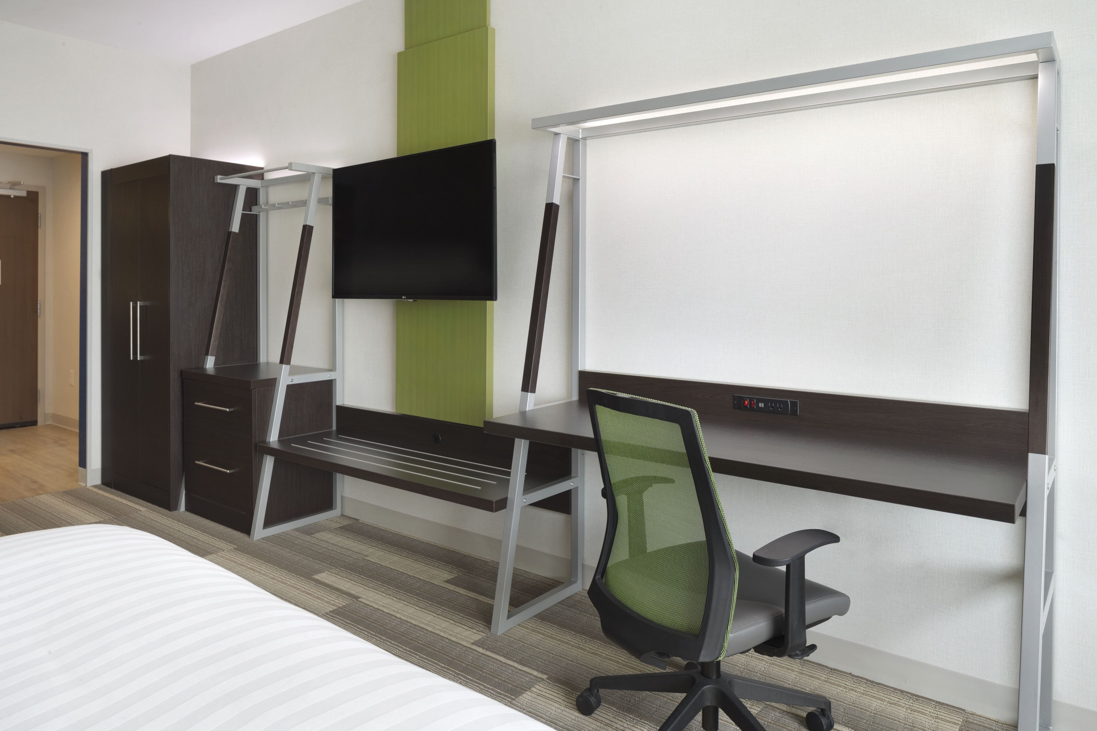 A hotel room with a bed, a desk with a chair, a TV, and a wardrobe.