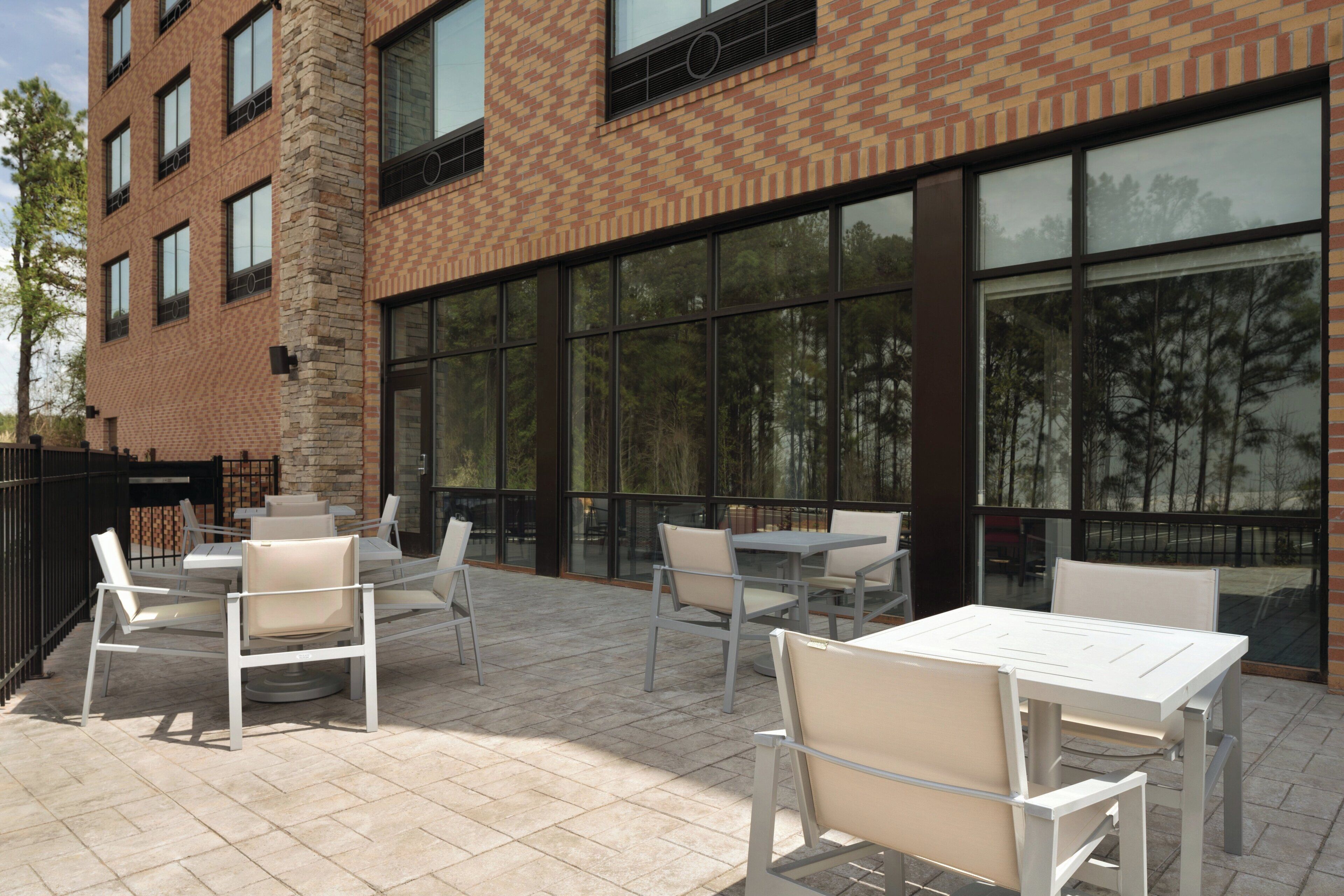 An outdoor patio with tables and chairs, large windows, and a brick building facade.