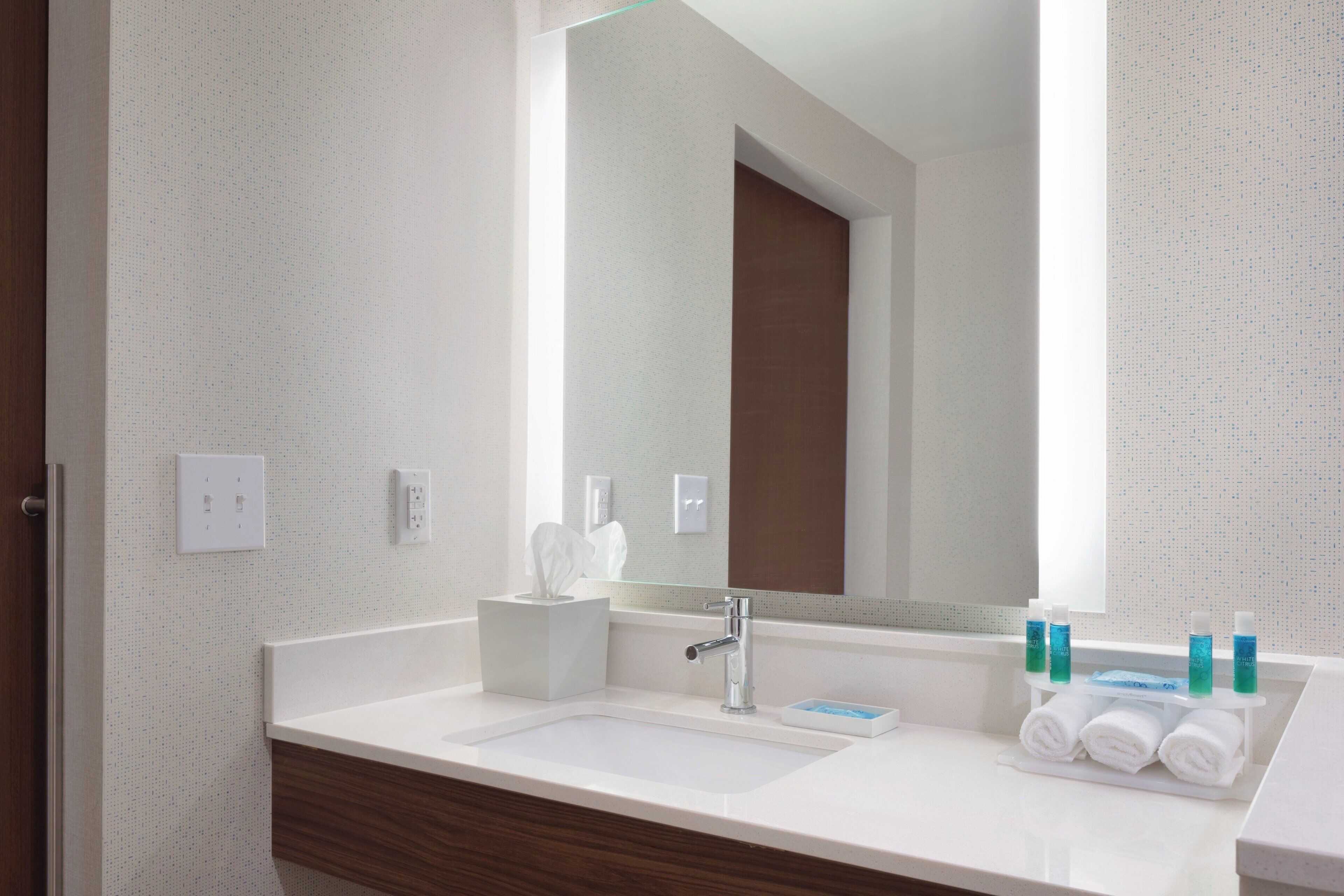 A modern bathroom with a white sink, a mirror, and toiletries.