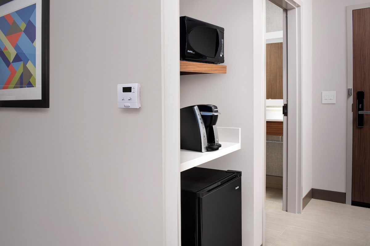 A modern kitchen with a microwave, coffee maker, and refrigerator on a white shelf.