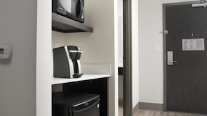 A hotel room with a microwave, coffee maker, and refrigerator on a white shelf. A door with an emergency evacuation plan is visible. - Holiday Inn Express Atlanta SW - Newnan by IHG (Newnan)