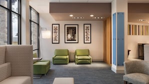 A hotel lobby with a carpeted floor, green armchairs, a sofa, and a large blue pillar. - Holiday Inn Express Atlanta SW - Newnan by IHG (Newnan)
