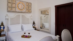 A neatly made bed with white linens and pillows, a tray with two glasses of wine, and a decorative mirror reflecting the room's interior. - Araújo Bazilio Pousada Tiradentes (Tiradentes)