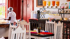 A restaurant interior with a bar area, wooden chairs, and a person in a white uniform. - Araújo Bazilio Pousada Tiradentes (Tiradentes)