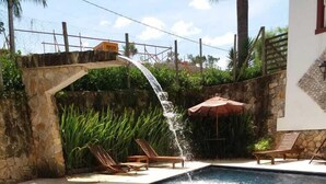 A swimming pool with a waterfall feature, surrounded by lounge chairs and a stone wall. - Araújo Bazilio Pousada Tiradentes (Tiradentes)