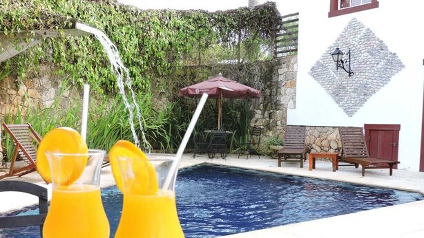 A pool area with two glasses of orange juice, a stone wall, and a wooden bench. - Araújo Bazilio Pousada Tiradentes (Tiradentes)