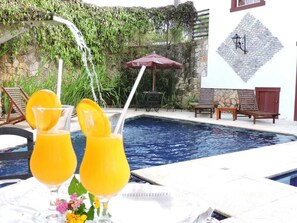A pool area with two glasses of orange juice, a stone wall, and a wooden bench. - Araújo Bazilio Pousada Tiradentes (Tiradentes)