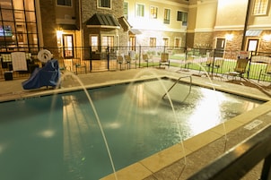 An indoor swimming pool with a covered slide, surrounded by a fence and chairs, with a building in the background.
