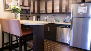 A modern kitchen with dark cabinets, stainless steel appliances, a dining area with a table and chairs, and a decorative vase on the counter. - Staybridge Suites Austin North - Parmer Lane by IHG (Austin)