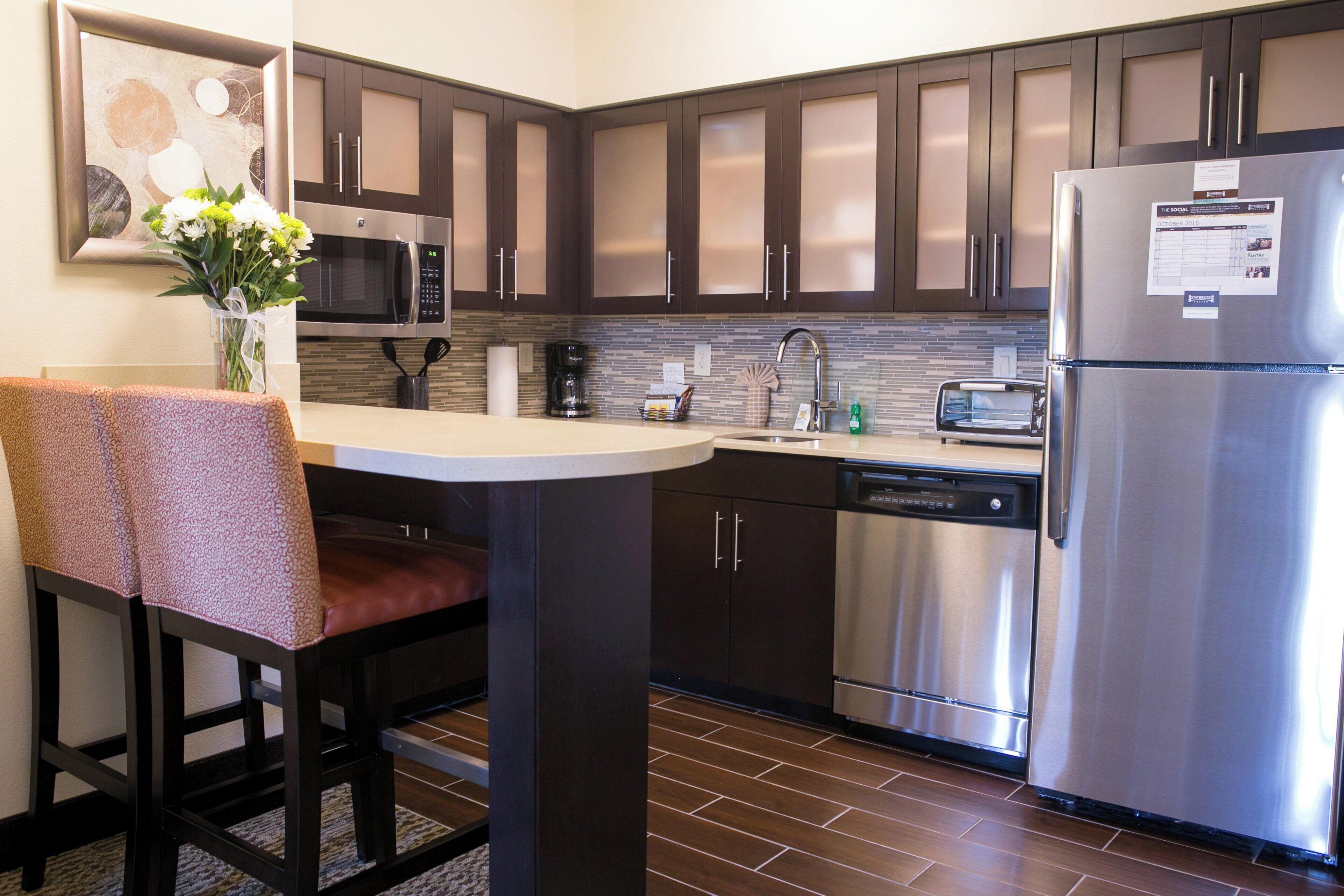 A modern kitchen with dark cabinets, stainless steel appliances, a dining area with a table and chairs, and a decorative vase on the counter.