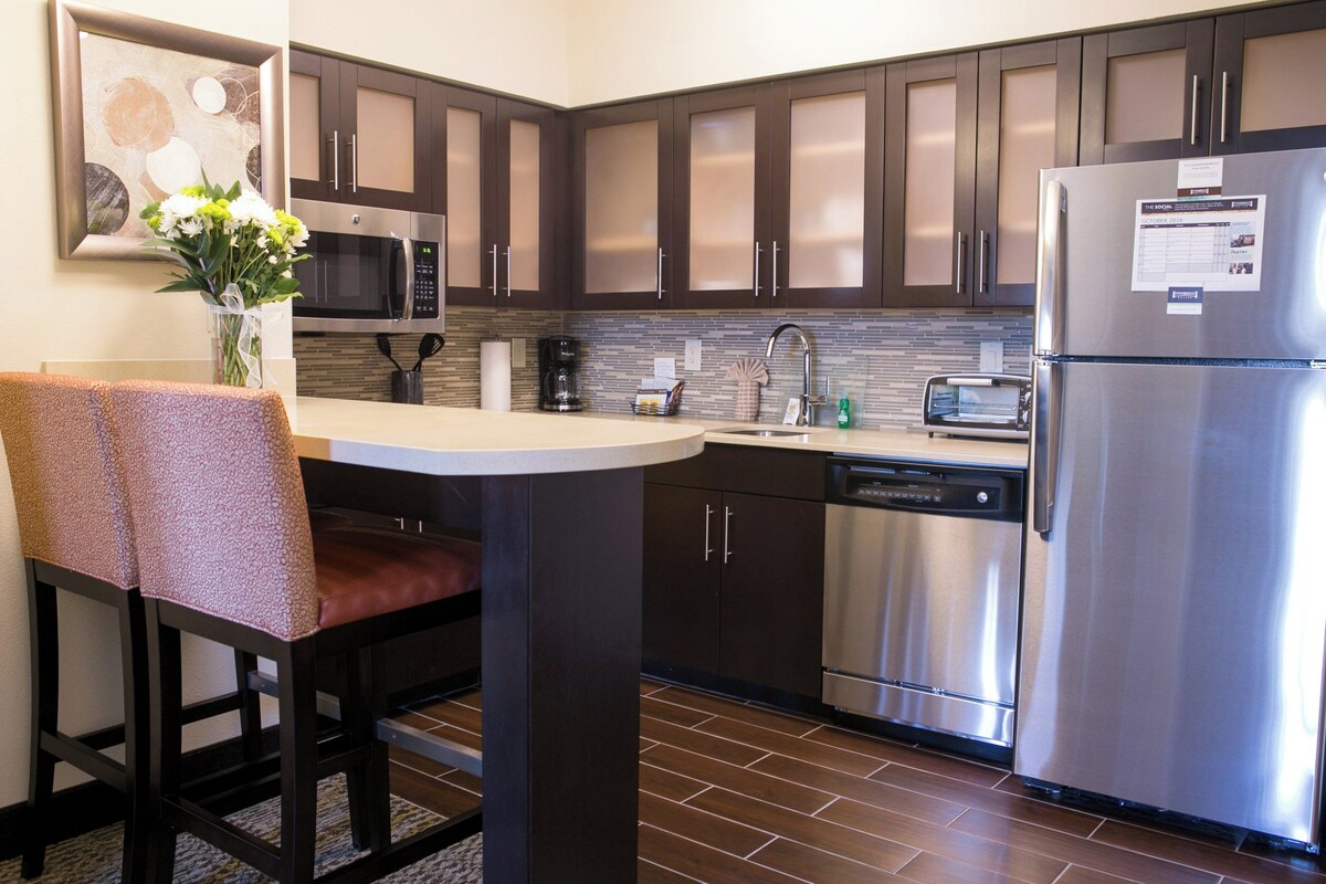 A modern kitchen with dark cabinets, stainless steel appliances, a dining area with a table and chairs, and a decorative vase on the counter.