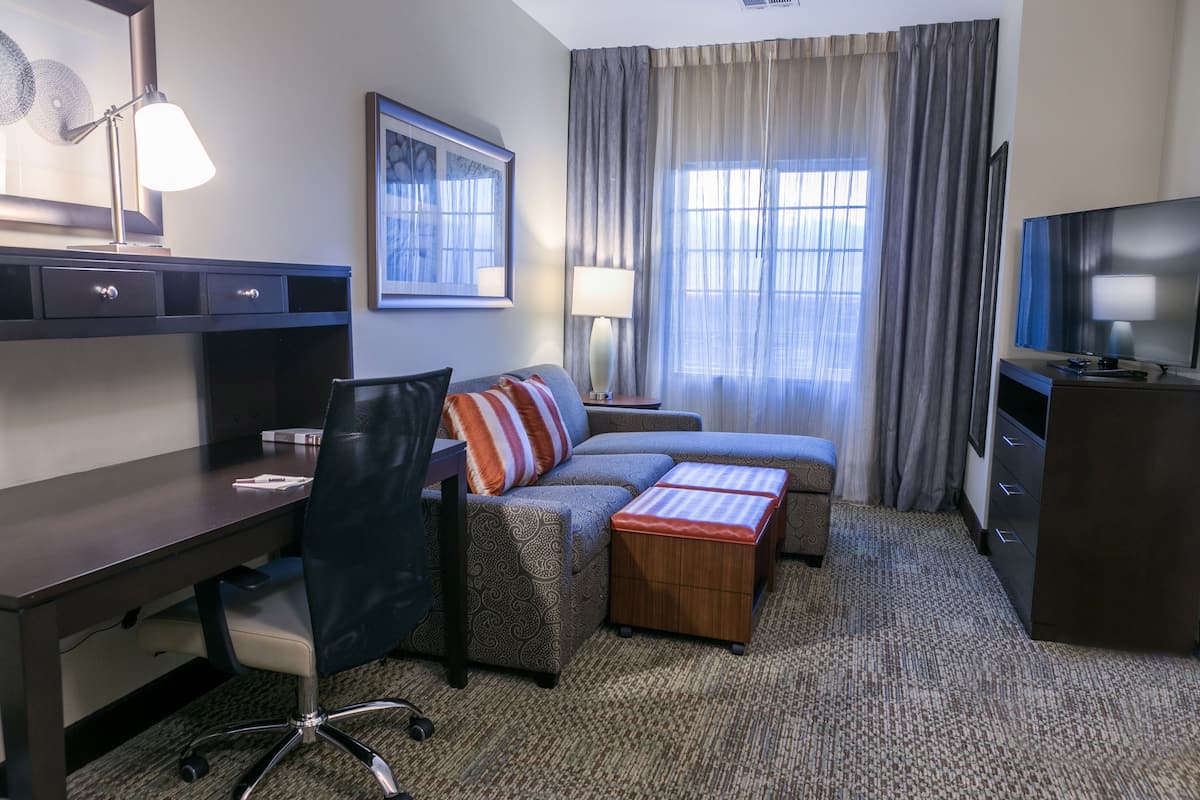 Een hotelkamer met een bureau, een bank, een televisie en een raam met gordijnen.