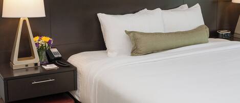 A hotel room with a bed, nightstand, lamp, phone, and a clock.