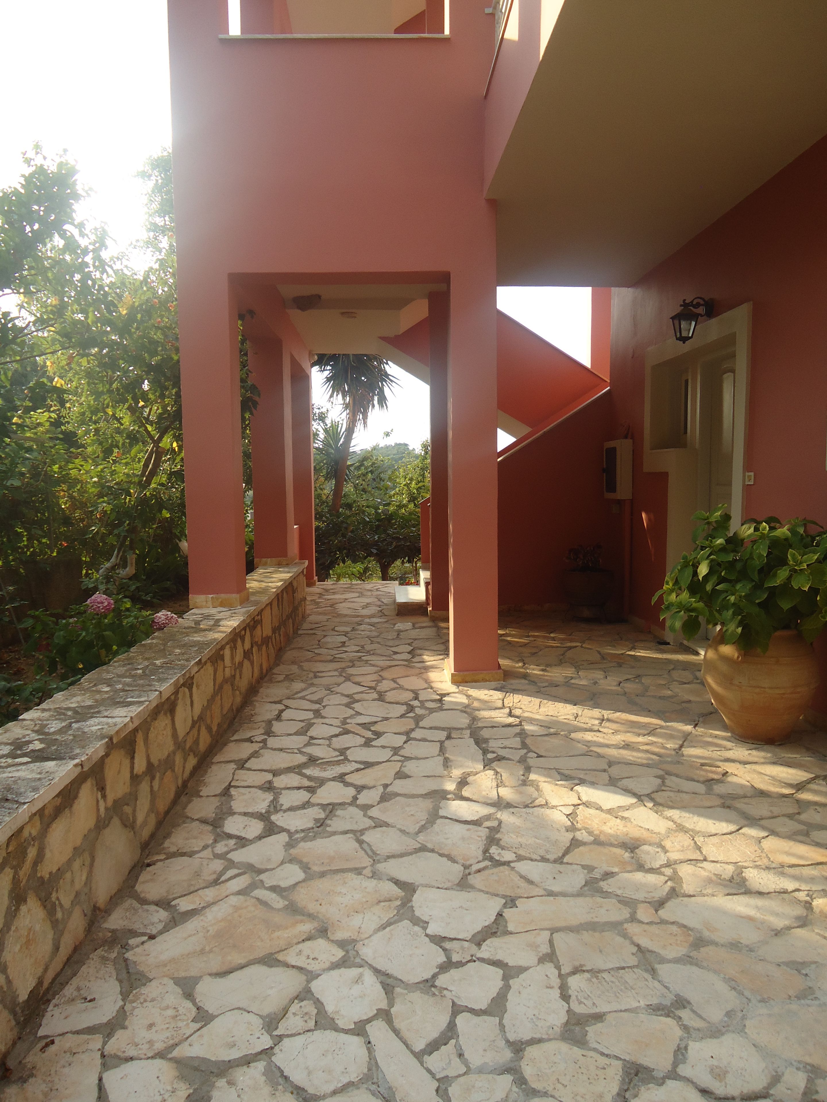 A stone-paved pathway leading to a building with pink walls and a potted plant.