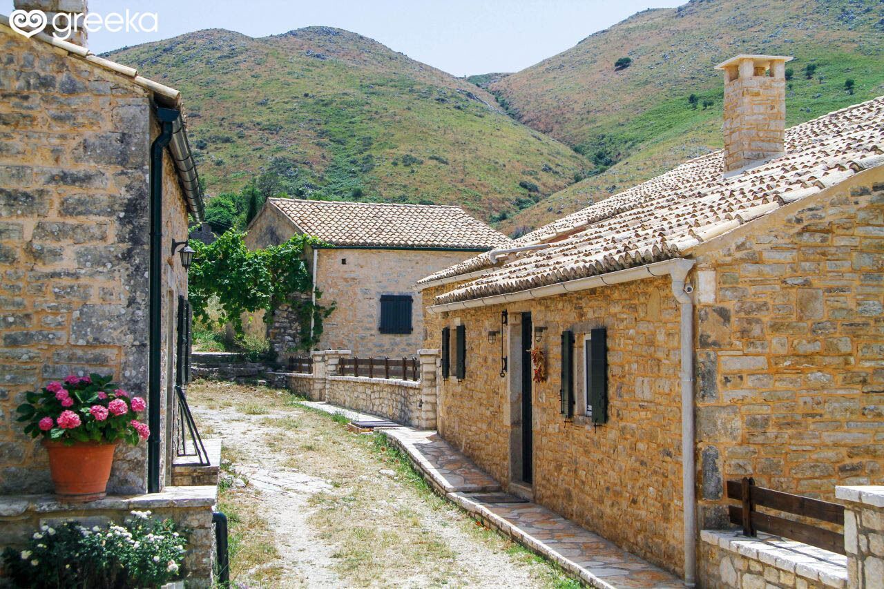 A stone building with a tiled roof, a stone pathway, and a mountainous backdrop.