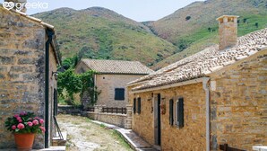 A stone building with a tiled roof, a stone pathway, and a mountainous backdrop. - Villa Bambas (Corfu)