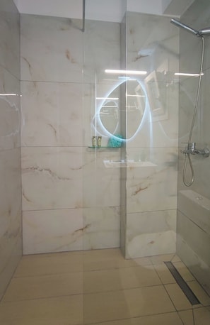 Eine gläserne Duschkabine mit Handbrause, ein Glasregal mit Toilettenartikeln und ein gefliester Boden.