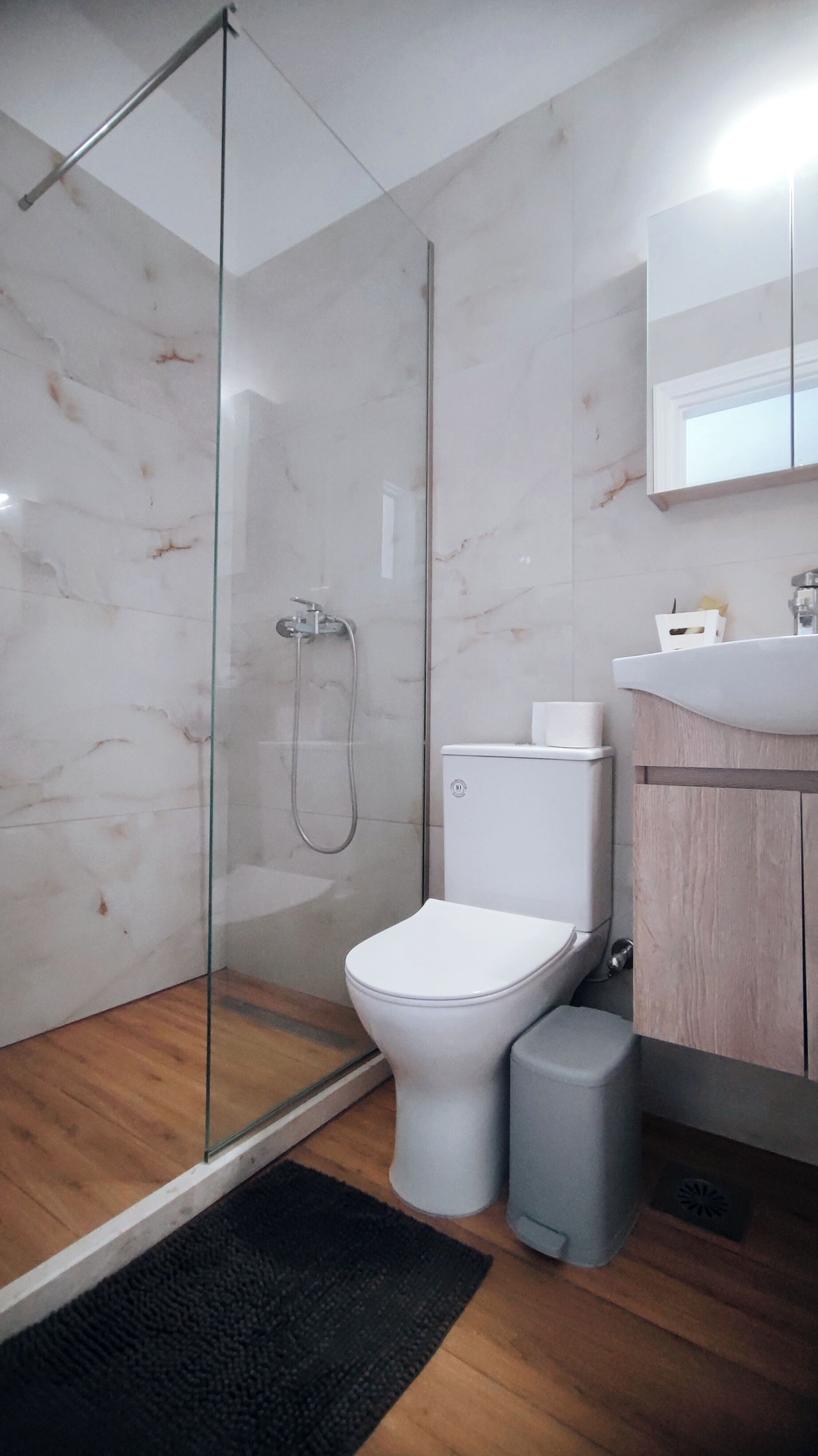 A modern bathroom with a glass-enclosed shower, a white toilet, and a wooden vanity.
