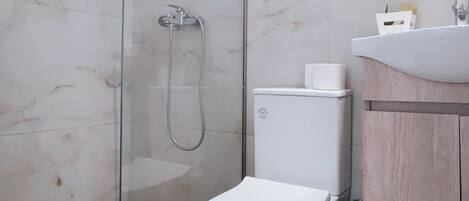 A modern bathroom with a glass-enclosed shower, a white toilet, and a wooden vanity.