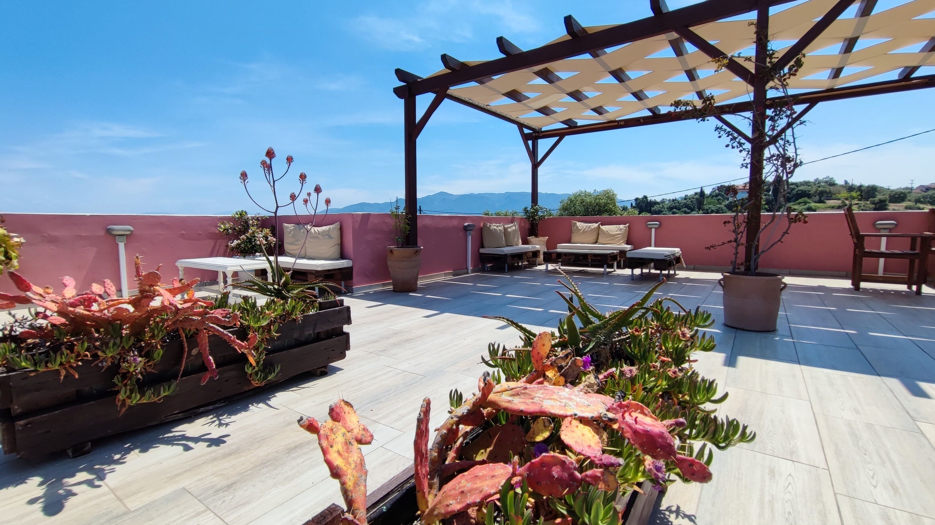 A rooftop terrace with a pergola, seating area, and potted plants.