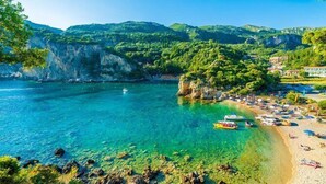 A coastal beach with clear water, a small boat, and a rocky shoreline. - Villa Bambas (Corfu)