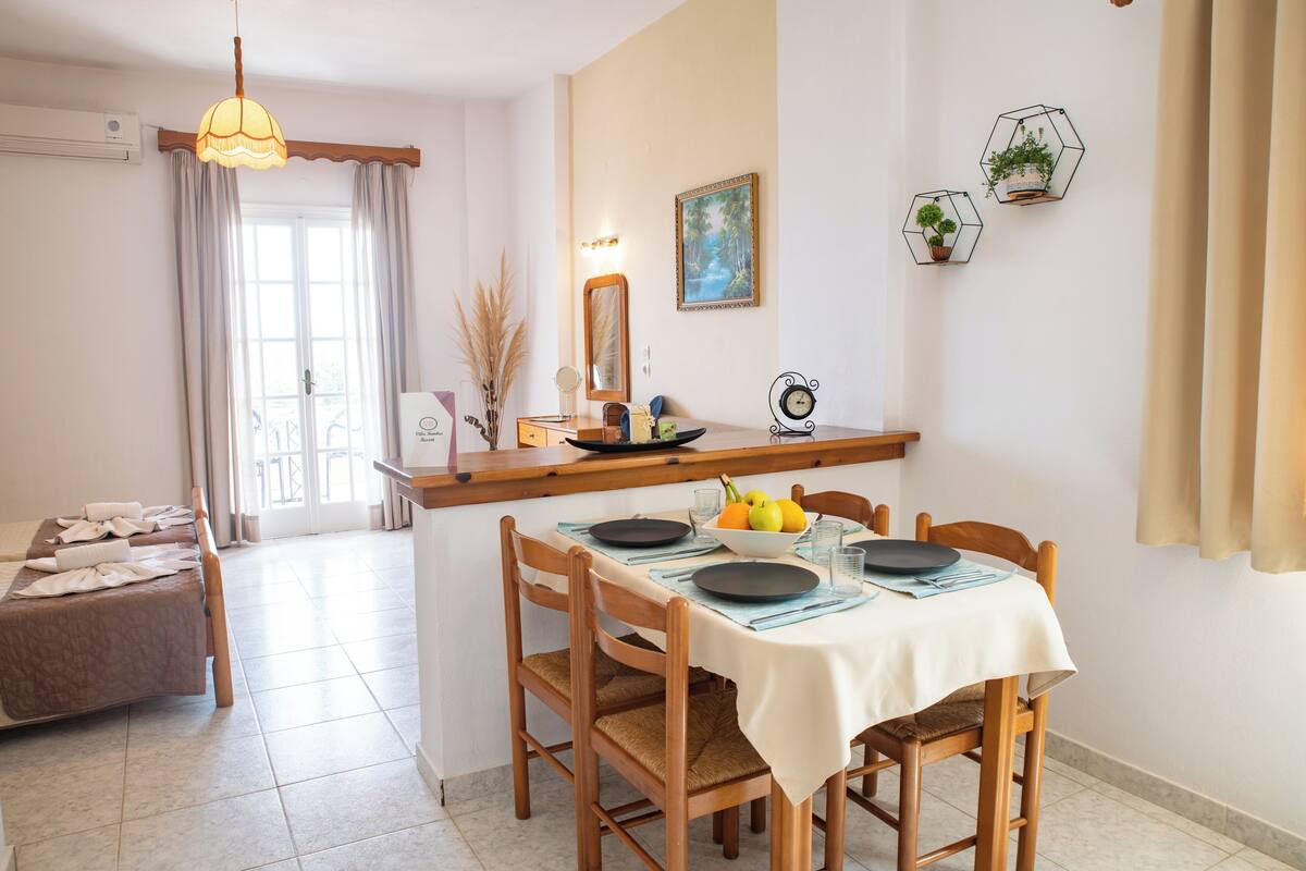 A dining area with a table set for four, a wooden chair, a hanging light fixture, and a window with curtains.