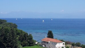 A coastal view with a building featuring a red-tiled roof, surrounded by greenery and overlooking the sea. - Villa Bambas (Corfu)
