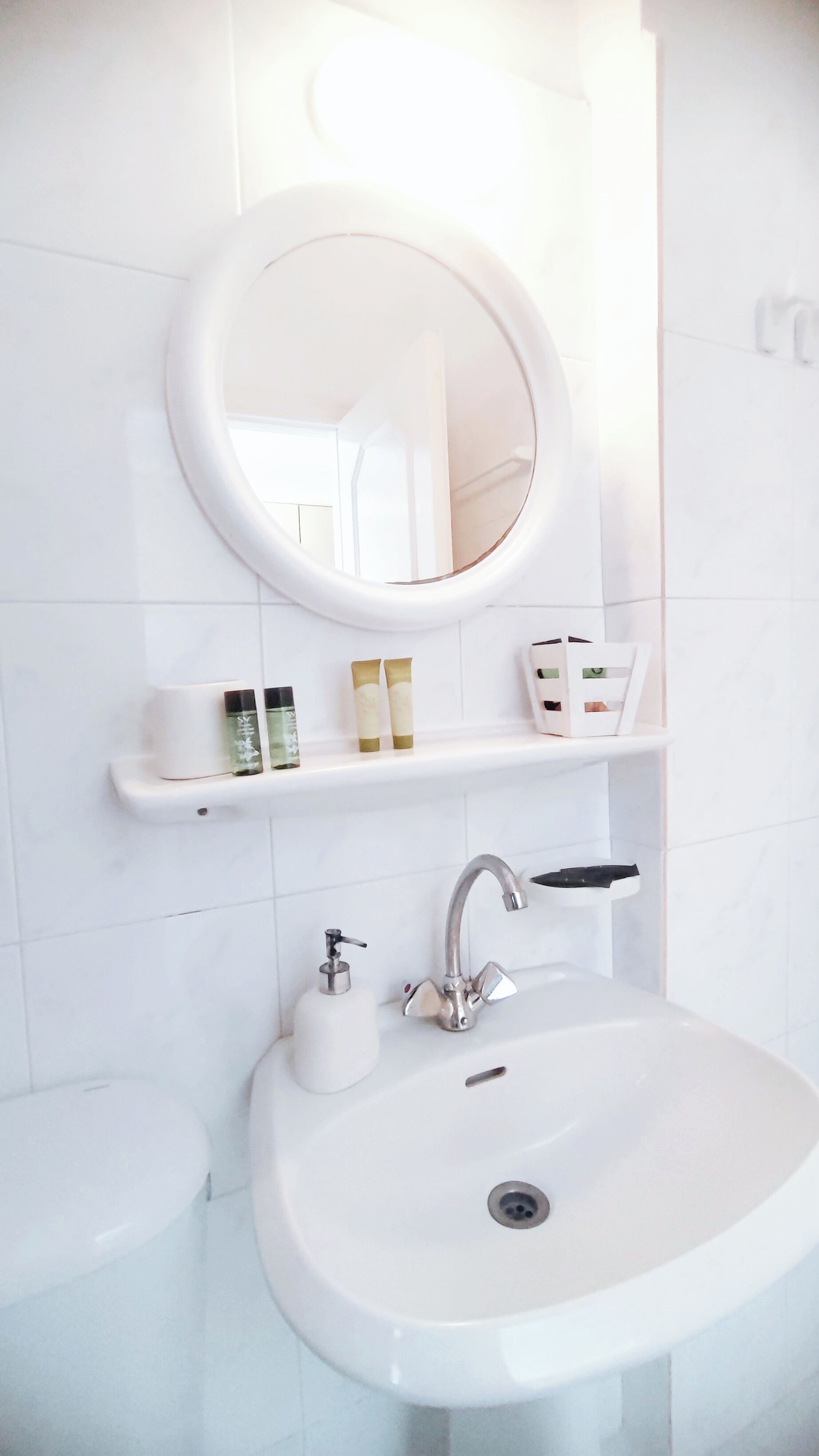 Un baño con un lavamanos blanco, un espejo redondo y una repisa con artículos de aseo.