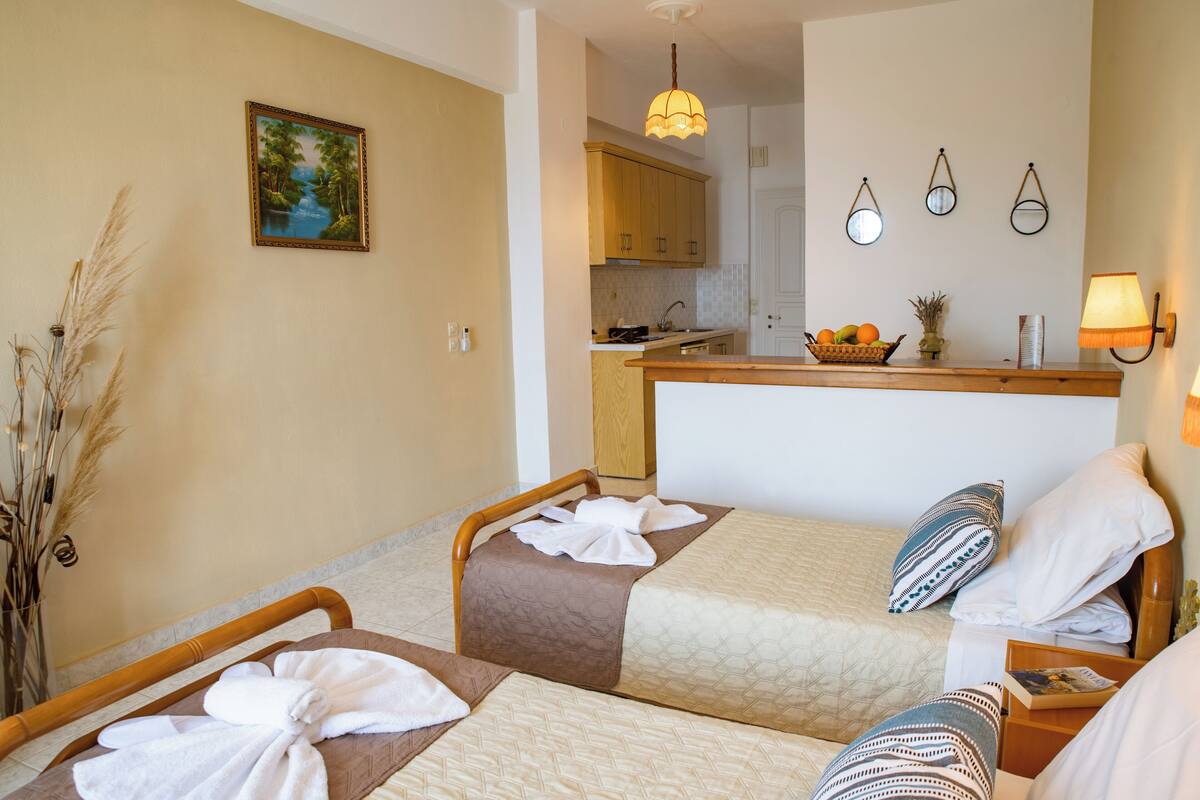 A hotel room with two beds, a small kitchenette, and a view of the kitchen.
