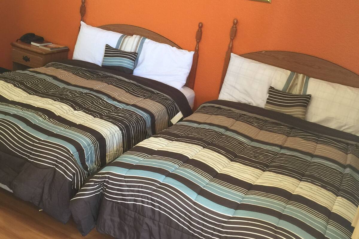 Uma cama de casal com roupa de cama listrada, uma mesinha de cabeceira com abajur e um quadro na parede.