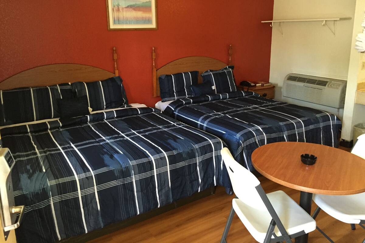 Quarto com duas camas, uma mesa de madeira redonda e uma cadeira branca.